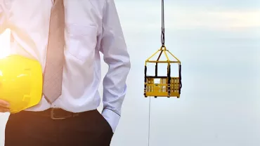 Person holding a yellow hard hat at a construction site with a crane in the background.