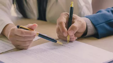 Two people reviewing documents with pens on a table.