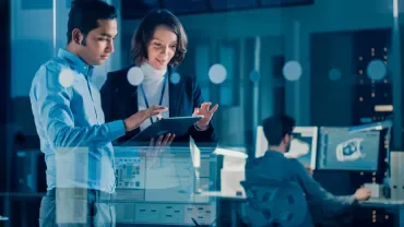 Two people reviewing information on a tablet in a modern office setting.