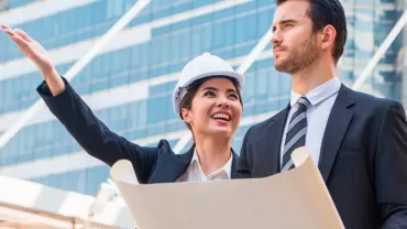 Two professionals with a blueprint in front of a modern building.