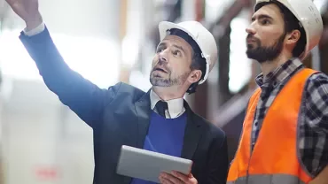 Two people in hard hats reviewing inventory in a warehouse.