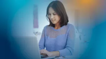 Person working on a laptop at a desk in a room.