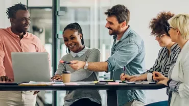 Group of people collaborating in an office setting with laptops and notes.