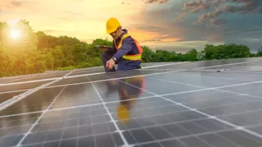 Person in helmet inspecting solar panels during sunset.