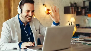 Person smiling and waving during a video call on a laptop.